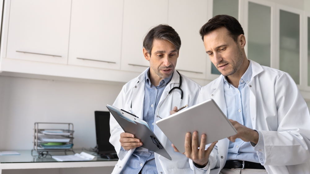 Dois médicos a analisar relatórios e resultados laboratoriais para avaliação pericial, destacando a diferença entre avaliação e tratamento.
